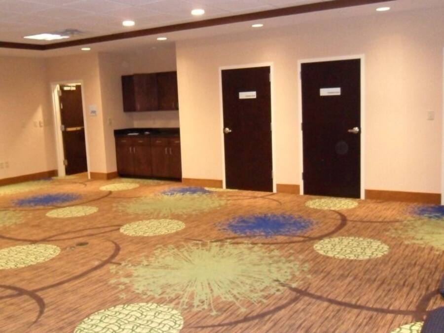 Un salón de conferencias con piso alfombrado, una kitchenette y una fila de sillas.