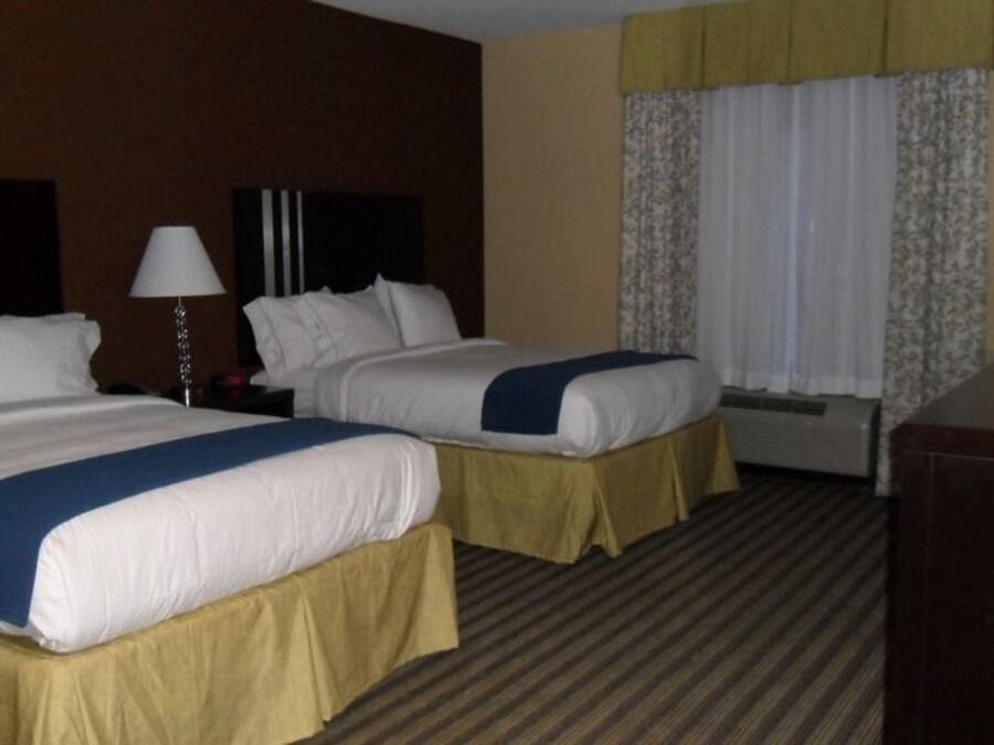 A hotel room with two beds, a desk, a lamp, and a window with curtains.