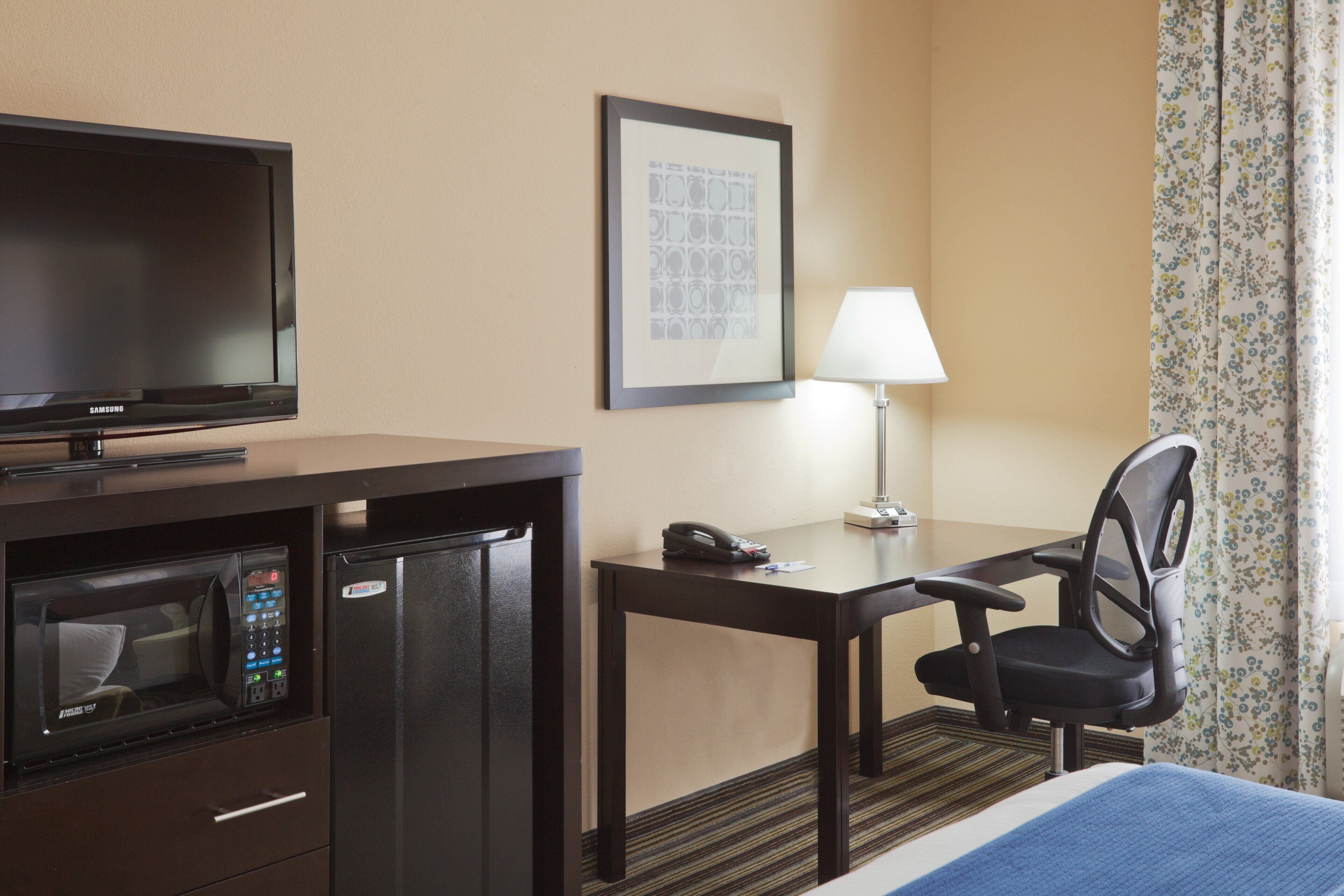 Une chambre d’hôtel équipée d’un lit, d’un bureau avec une chaise, d’une télévision, d’un four à micro-ondes et d’un téléphone.