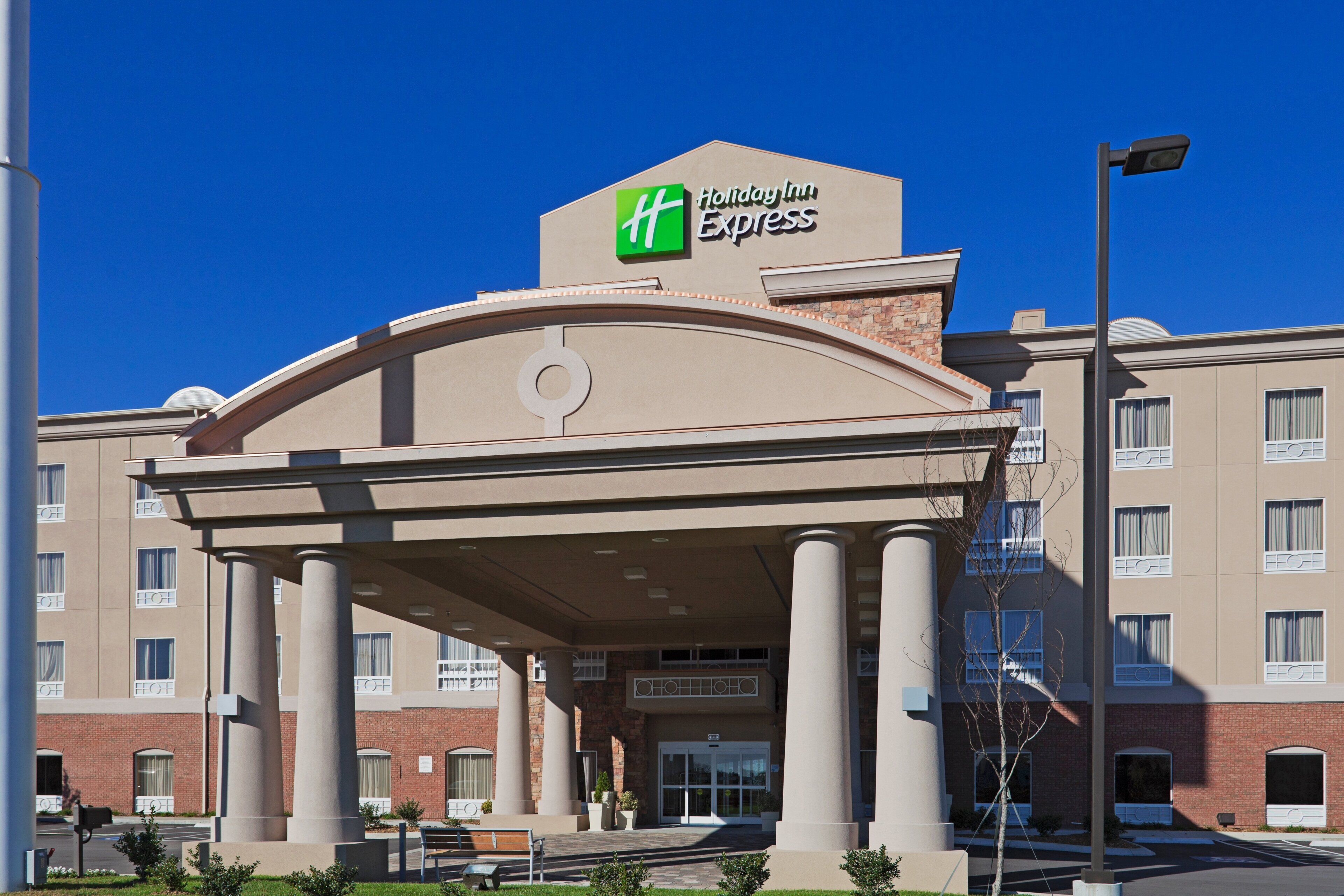 Un bâtiment de l’hôtel Holiday Inn Express avec une entrée centrale, des colonnes et un ciel bleu dégagé.