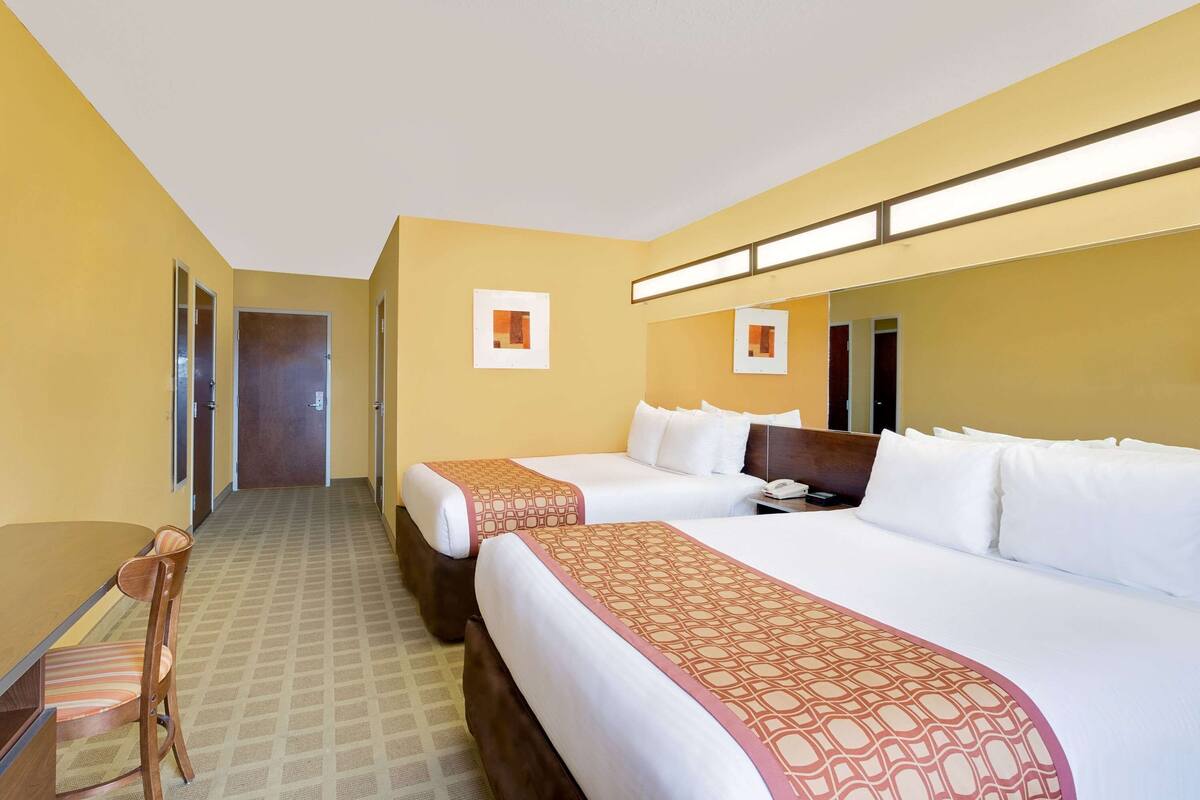 A hotel room with two beds, a desk, and a chair. There are doors leading to other rooms and a bathroom.