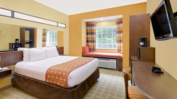 A hotel room with a large bed, a desk, a TV, and a window with curtains. - Microtel Inn & Suites by Wyndham Princeton (Princeton)