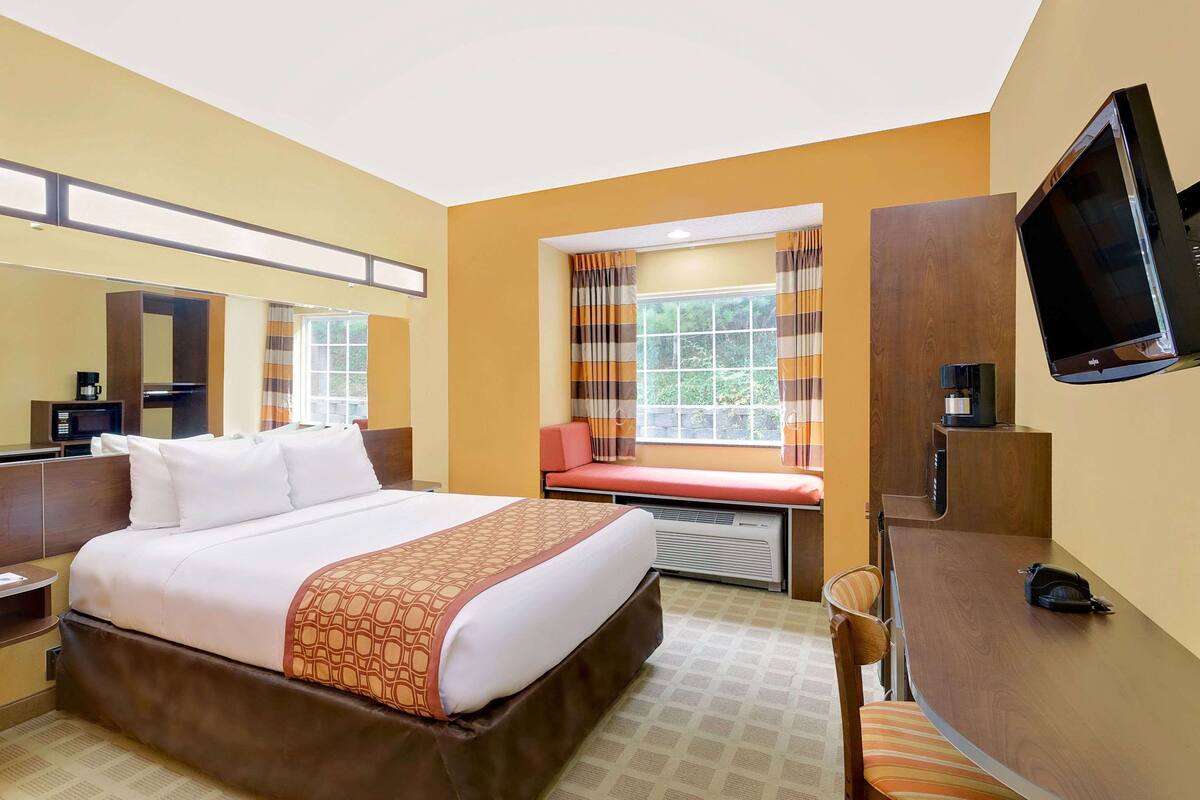 A hotel room with a large bed, a desk, a TV, and a window with curtains.