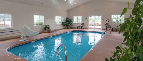 An indoor swimming pool with clear water, surrounded by potted plants, and equipped with a ceiling fan and recessed lighting.