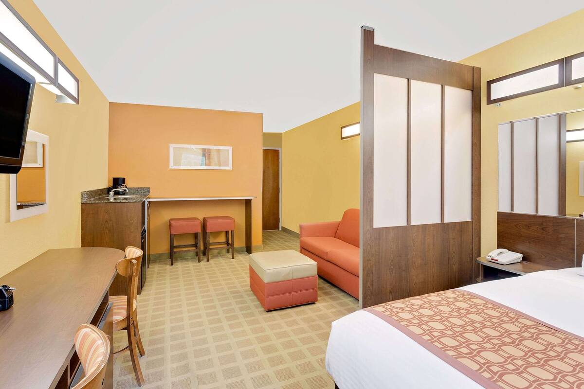 A hotel room with a bed, a desk, a chair, a small table, a sofa, and a TV.