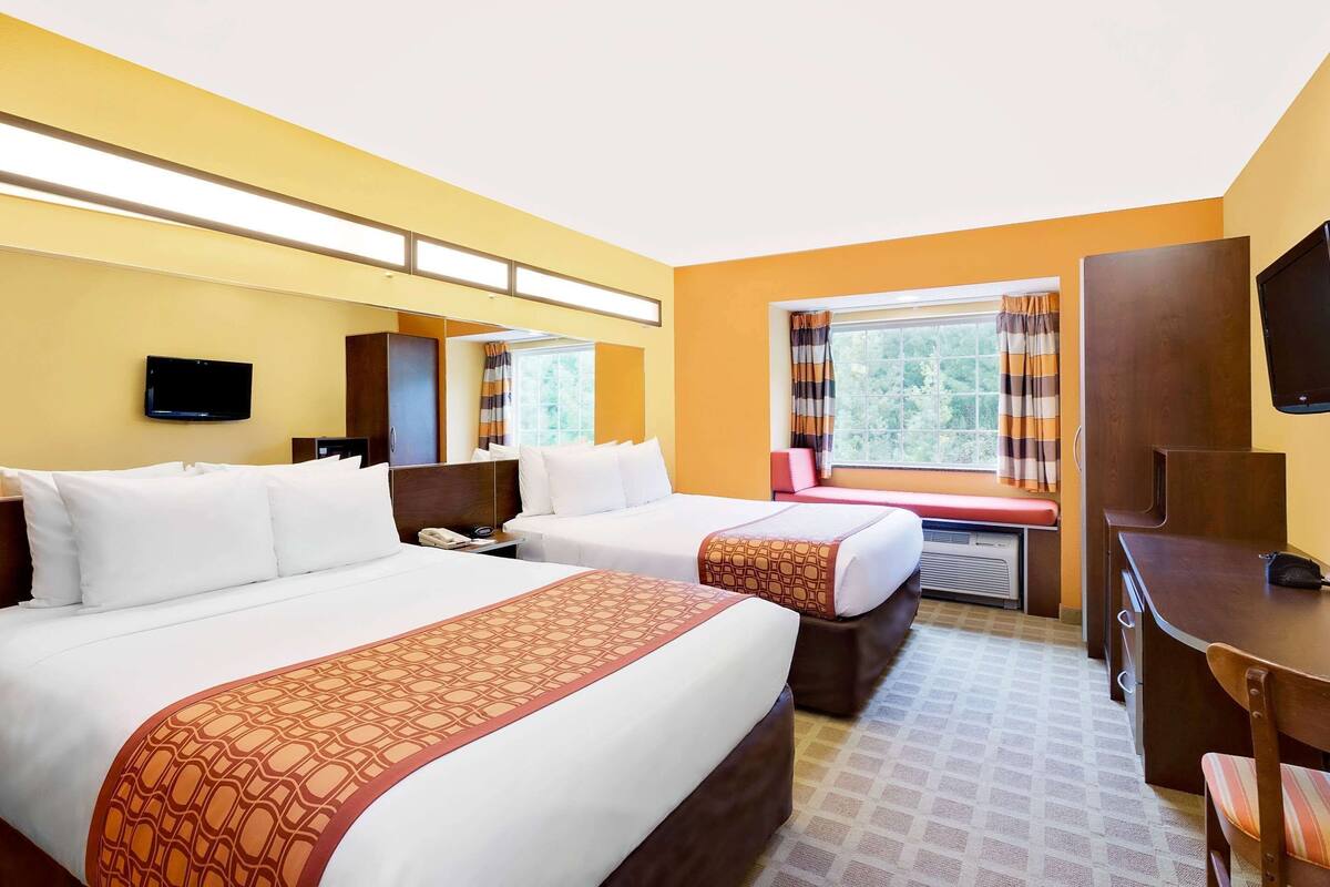 A hotel room with two beds, a desk, a chair, a TV, and a window with curtains.