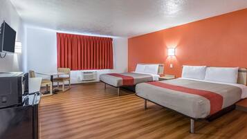 A hotel room with two beds, a desk, a chair, a TV, and a window with red curtains.
