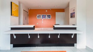 A reception area with two counters, a bulletin board with photos, and a sign encouraging saving money for travel.