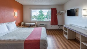 A hotel room with a bed, a desk, a chair, a TV, and a window with a view of trees.