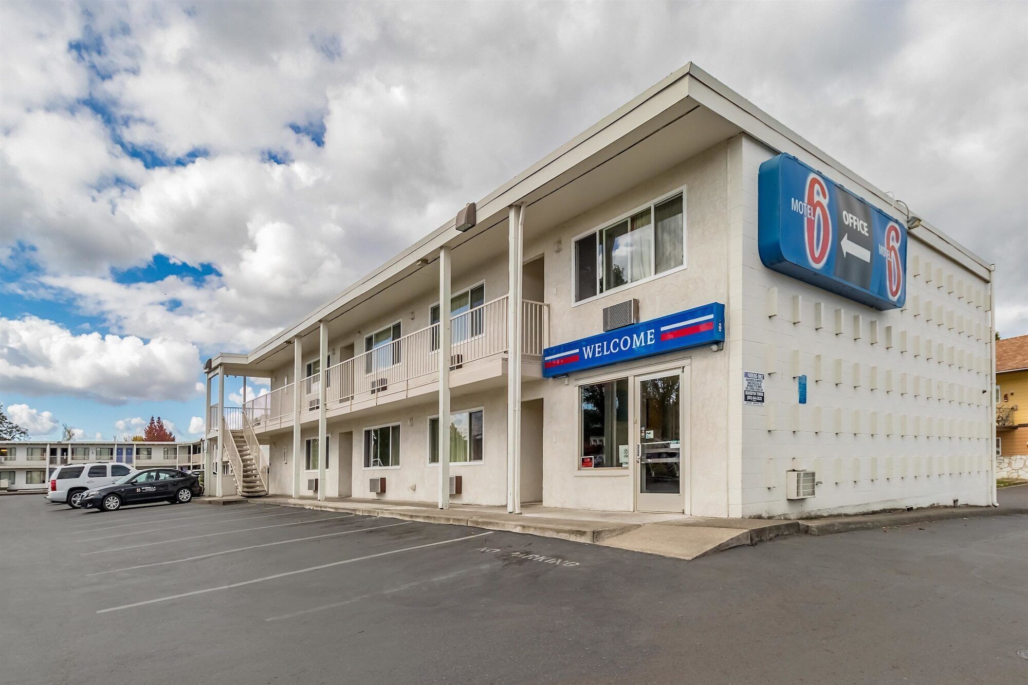 A motel with a 'Welcome' sign, a parking lot, and a 'No Parking' sign on the street.