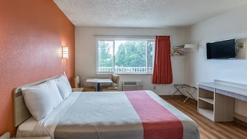 A hotel room with a bed, a desk, a chair, a TV, and a window with a view of trees.