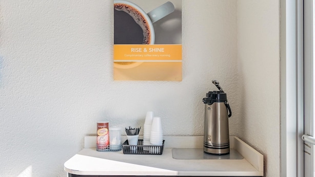 A coffee station with a coffee creamer can, disposable cups, a coffee grinder, and a stainless steel thermos.