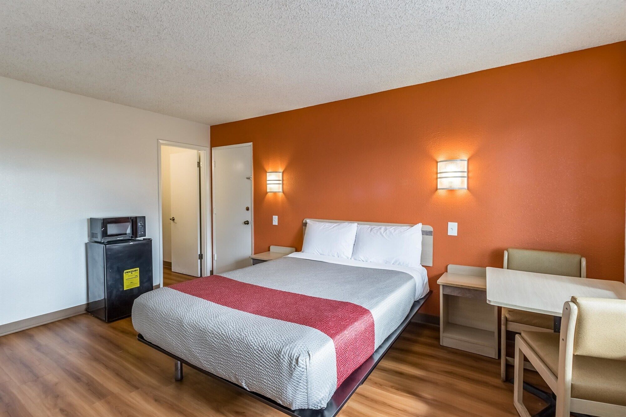 A hotel room with a bed, a desk, a chair, and a microwave.