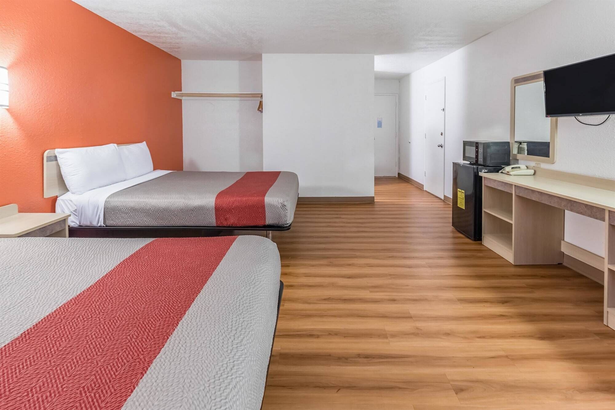 A hotel room with two beds, a desk with a computer, a television, and a refrigerator.