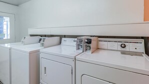 A laundry room with three stacked washers and dryers, a control panel, and a window with a view of buildings outside.