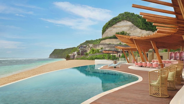 A poolside area with a wooden deck, lounge chairs, and a view of the beach and ocean. - Umana Bali, LXR Hotels & Resorts (Ungasan)