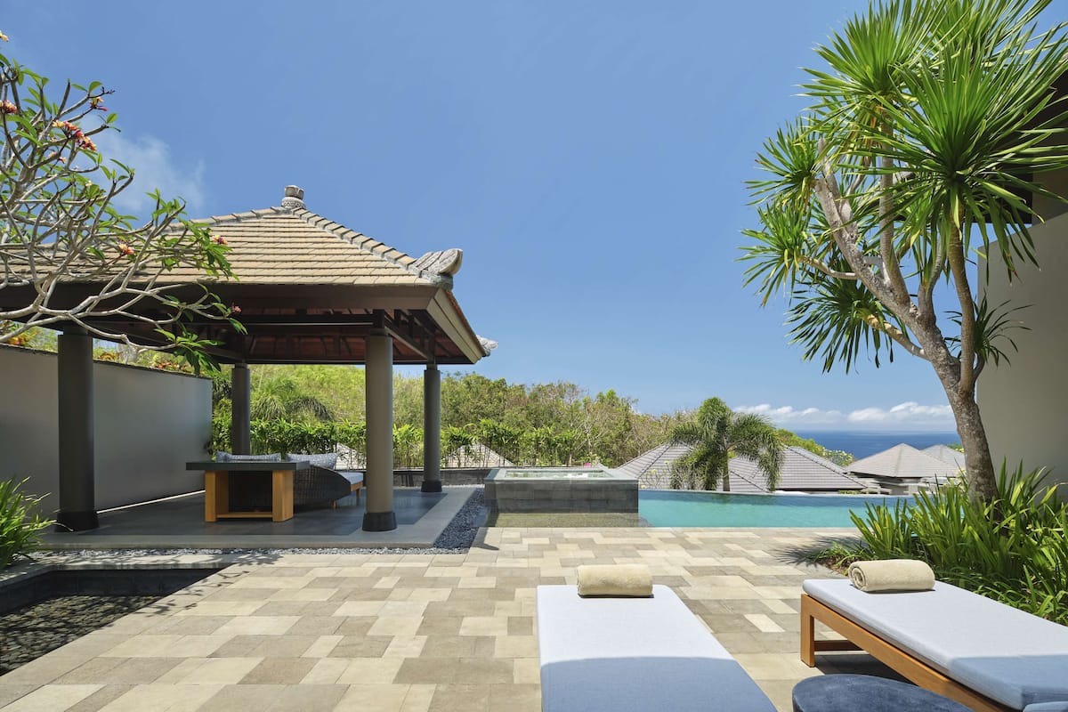 A poolside area with lounge chairs, a hot tub, and a gazebo overlooking a pool and ocean view.