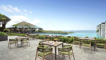 An outdoor dining area with tables and chairs, overlooking a pool and ocean view.
