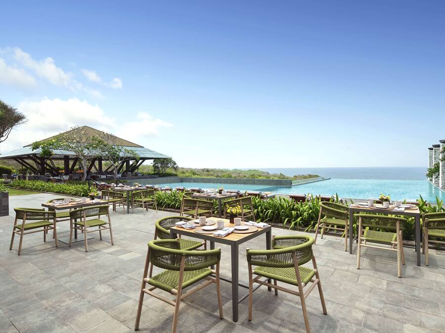 An outdoor dining area with tables and chairs, overlooking a pool and ocean view.