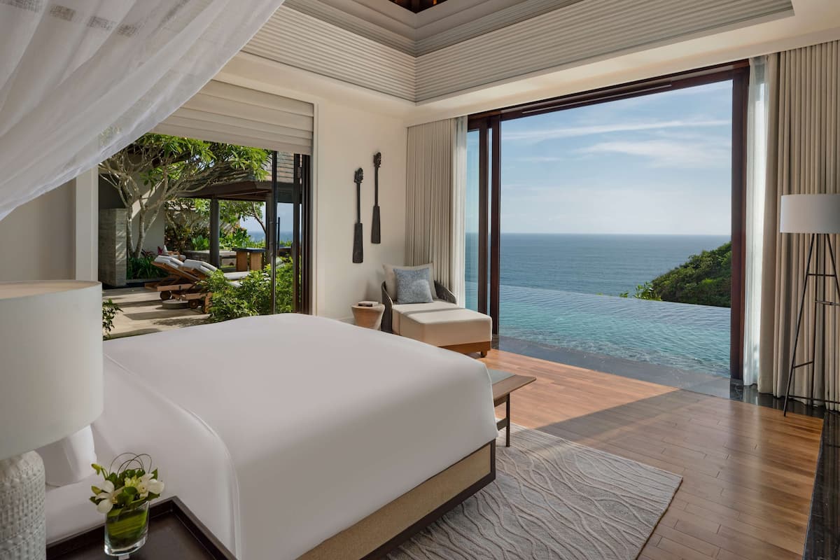 A spacious bedroom with a large bed, a view of the ocean, and a balcony with outdoor furniture.