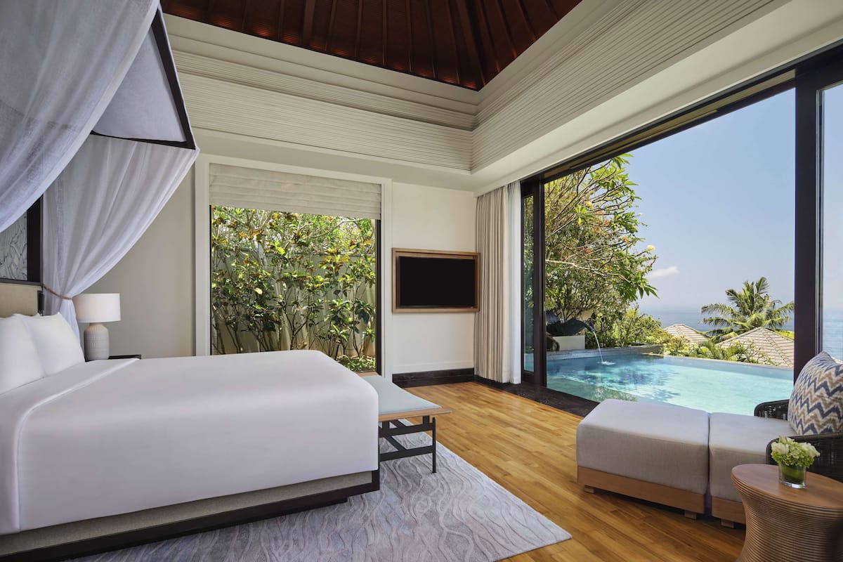 A bedroom with a large bed, a sofa, a TV, and a view of an infinity pool and ocean.