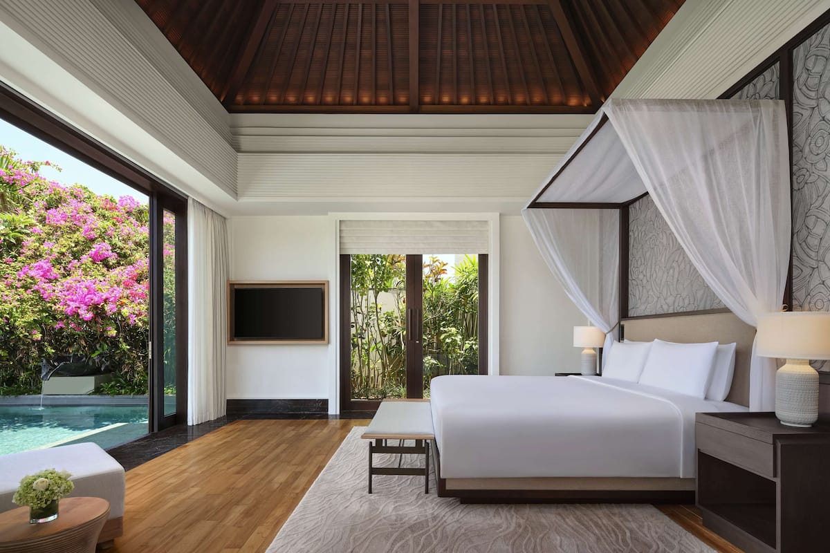 A modern bedroom with a large bed, bedside tables, a TV, and a view of a swimming pool and garden.