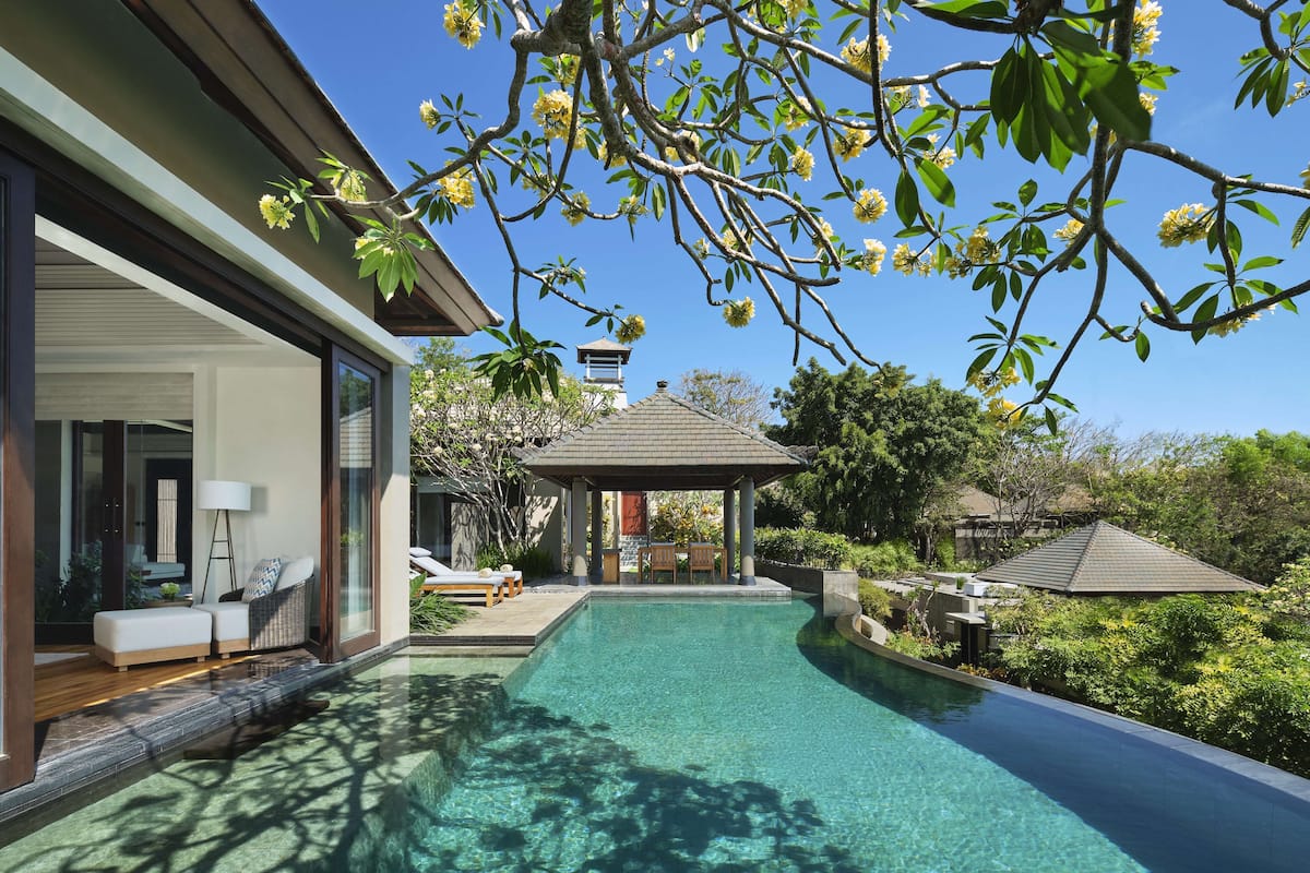 A modern house with a swimming pool, a covered patio, and a view of the surrounding greenery.