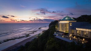 A coastal hotel with a glass conservatory overlooking the sea, a dining area with outdoor seating, and a modern building with a green roof. - Umana Bali, LXR Hotels & Resorts (Ungasan)