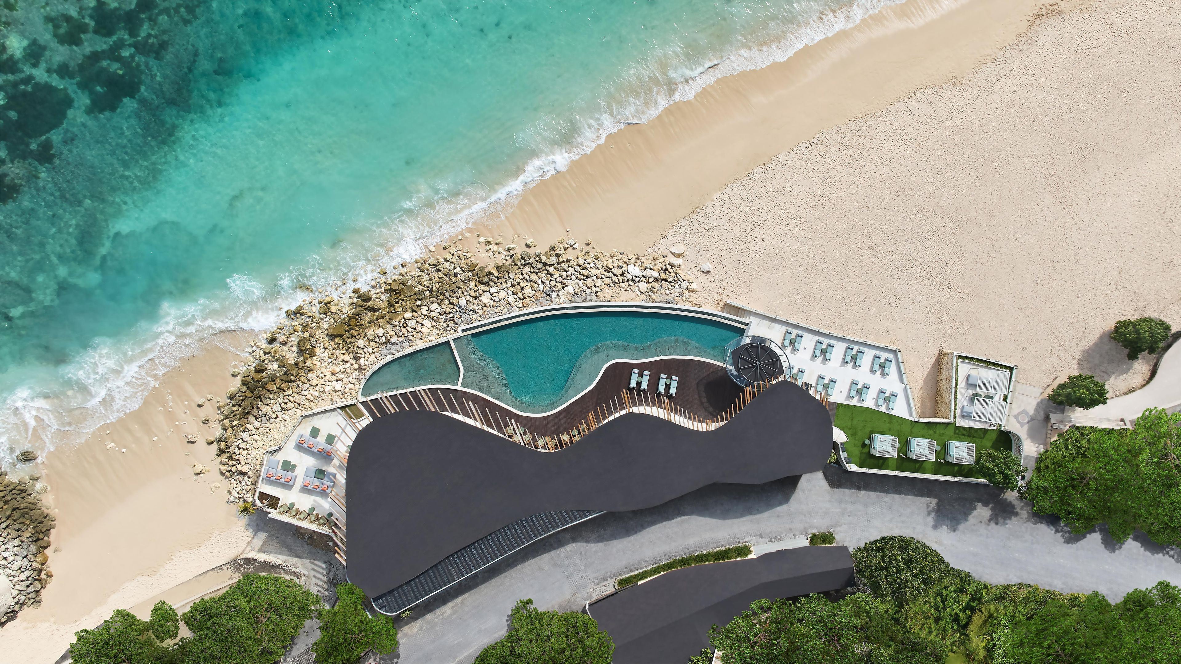 An aerial view of a resort with a swimming pool, beach, and landscaped areas.