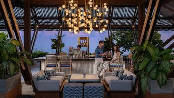 Un espace bar extérieur avec des sièges, un barman et une vue sur le ciel.
