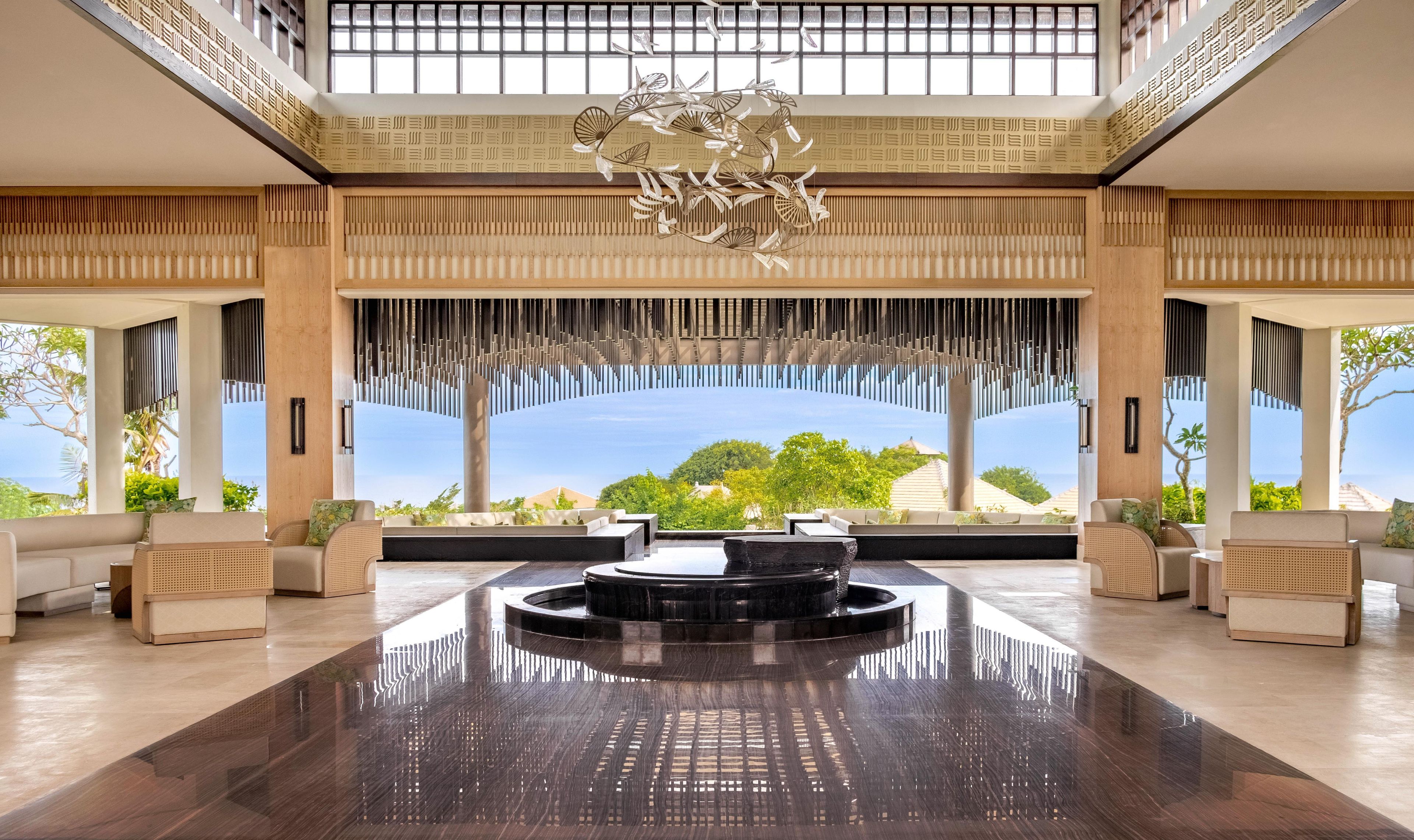 A spacious lobby with a central water feature, seating areas, and large windows offering a view of the sea.