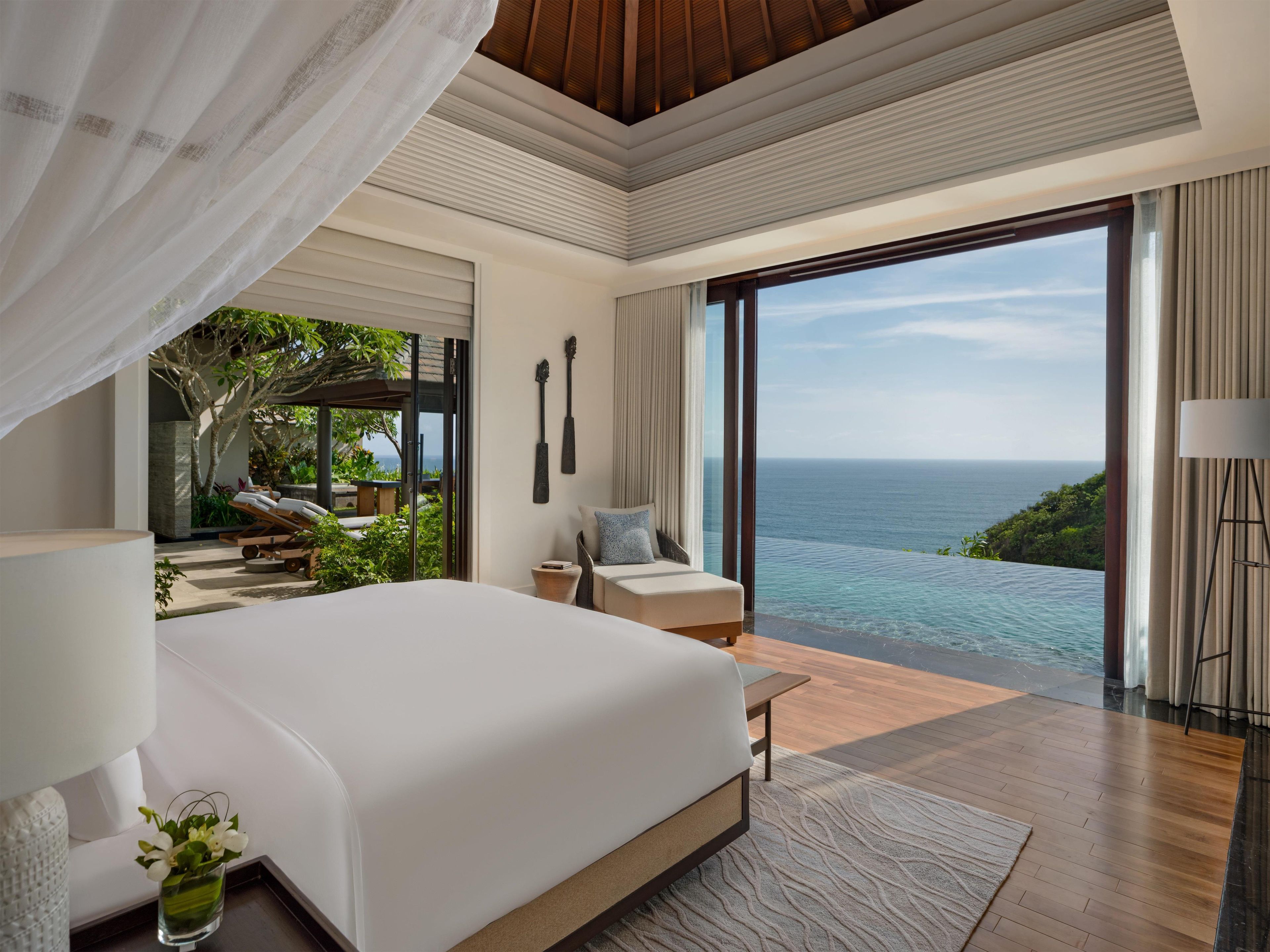 A modern bedroom with a large bed, a view of the ocean, and a balcony with outdoor furniture.