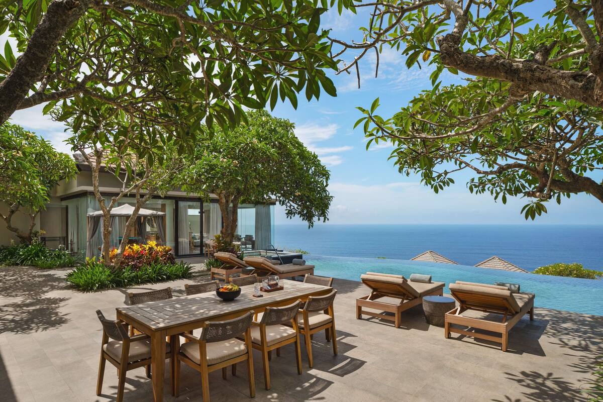 A luxurious outdoor seating area with a view of the ocean, featuring a dining table and lounge chairs.
