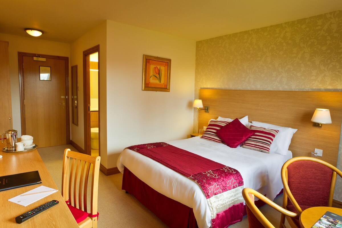 Ein Hotelzimmer mit einem Bett, einem Schreibtisch mit Stuhl, einer Fernbedienung und einer Lampe.