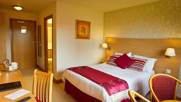 A hotel room with a large bed, a desk with a chair, a remote control, and a framed picture on the wall.