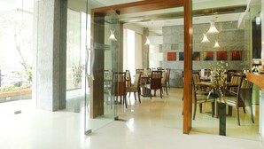A spacious hotel lobby with a modern design, featuring a glass partition, a wooden reception desk, and a dining area with chairs and tables. - Regency Hotel Malabar Hill (Mumbai)