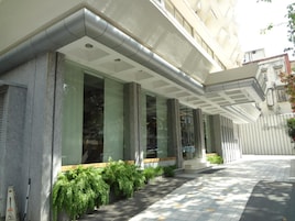 Un edificio moderno con ventanas amplias, un acceso cubierto y un paseo con baldosas.