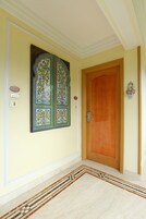 Un pasillo con puerta de madera, un panel decorativo en la pared y suelo de mármol.