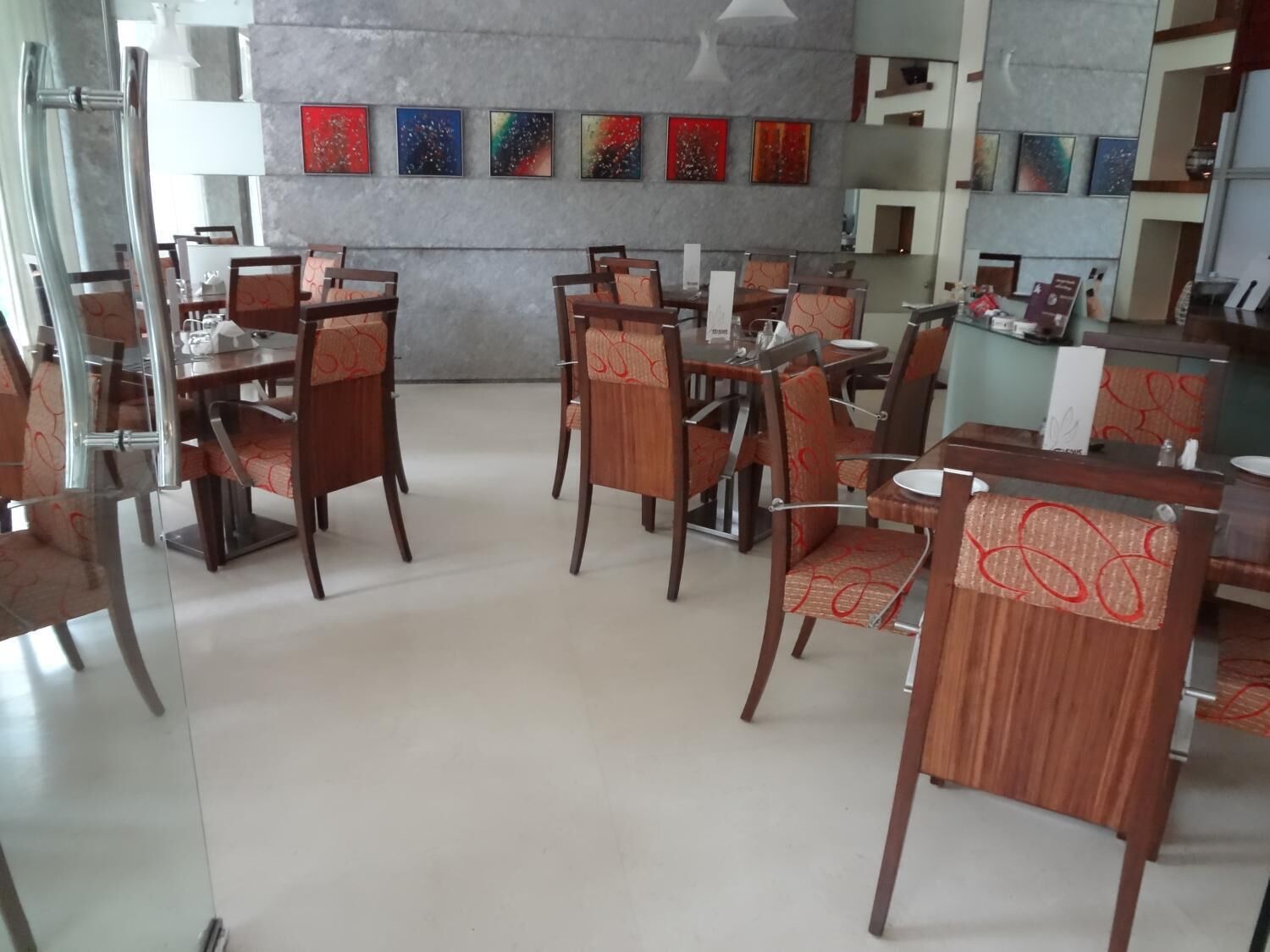 Un comedor con mesas y sillas de madera, una pared gris con obras de arte coloridas y un diseño interior moderno.