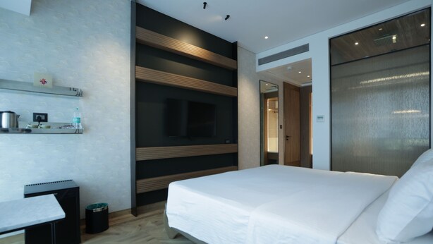 A modern hotel room with a large bed, a desk, a TV mounted on the wall, and a bathroom visible through an open door. - Regency Hotel Malabar Hill (Mumbai)