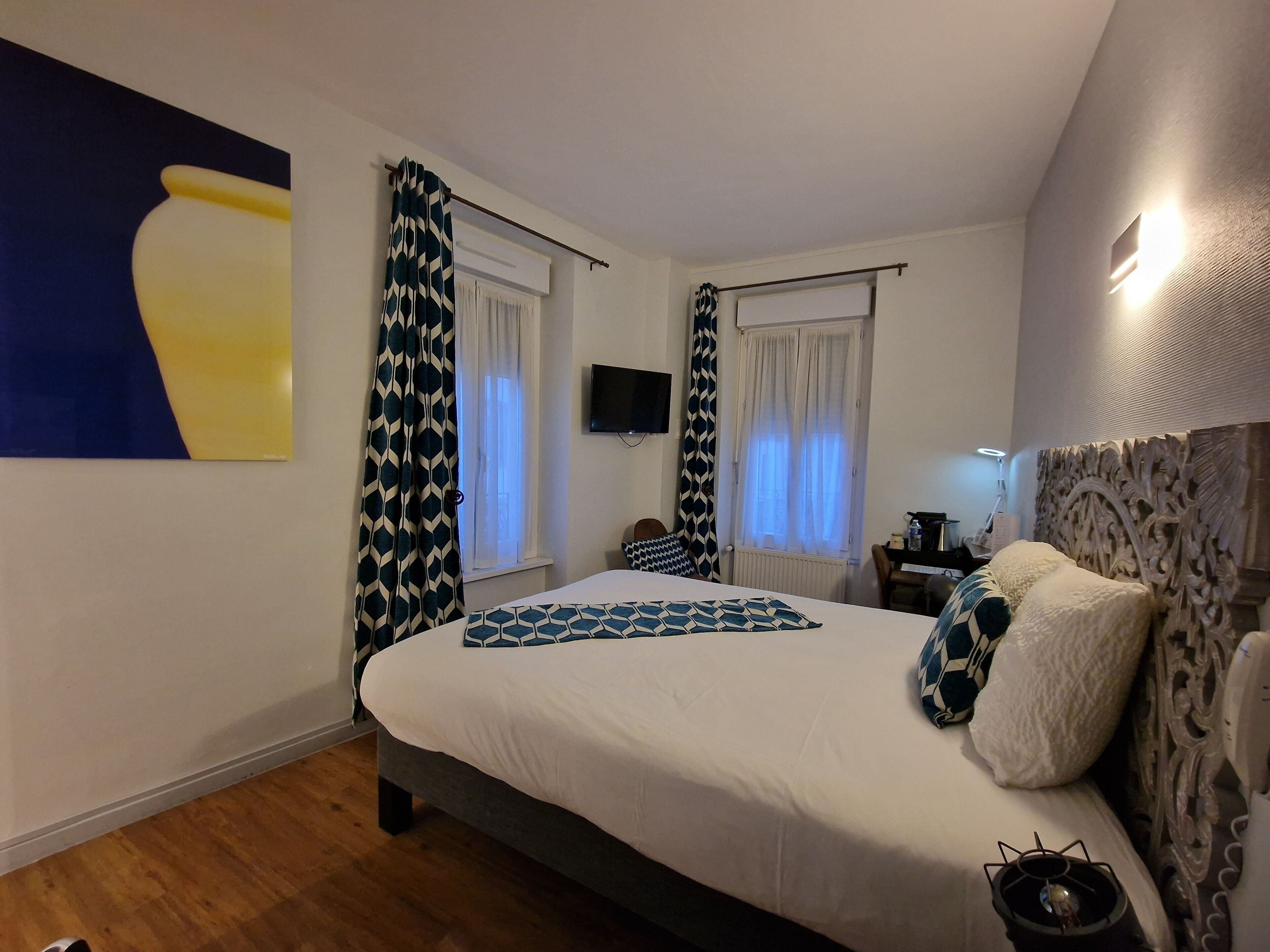 Un dormitorio con cama, cortinas, televisor y una lámpara de pared.