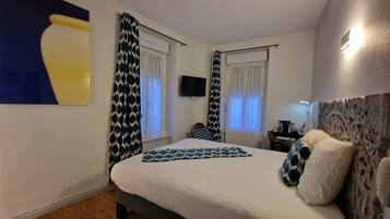 Un dormitorio con cama, cortinas, televisor y una lámpara de pared.