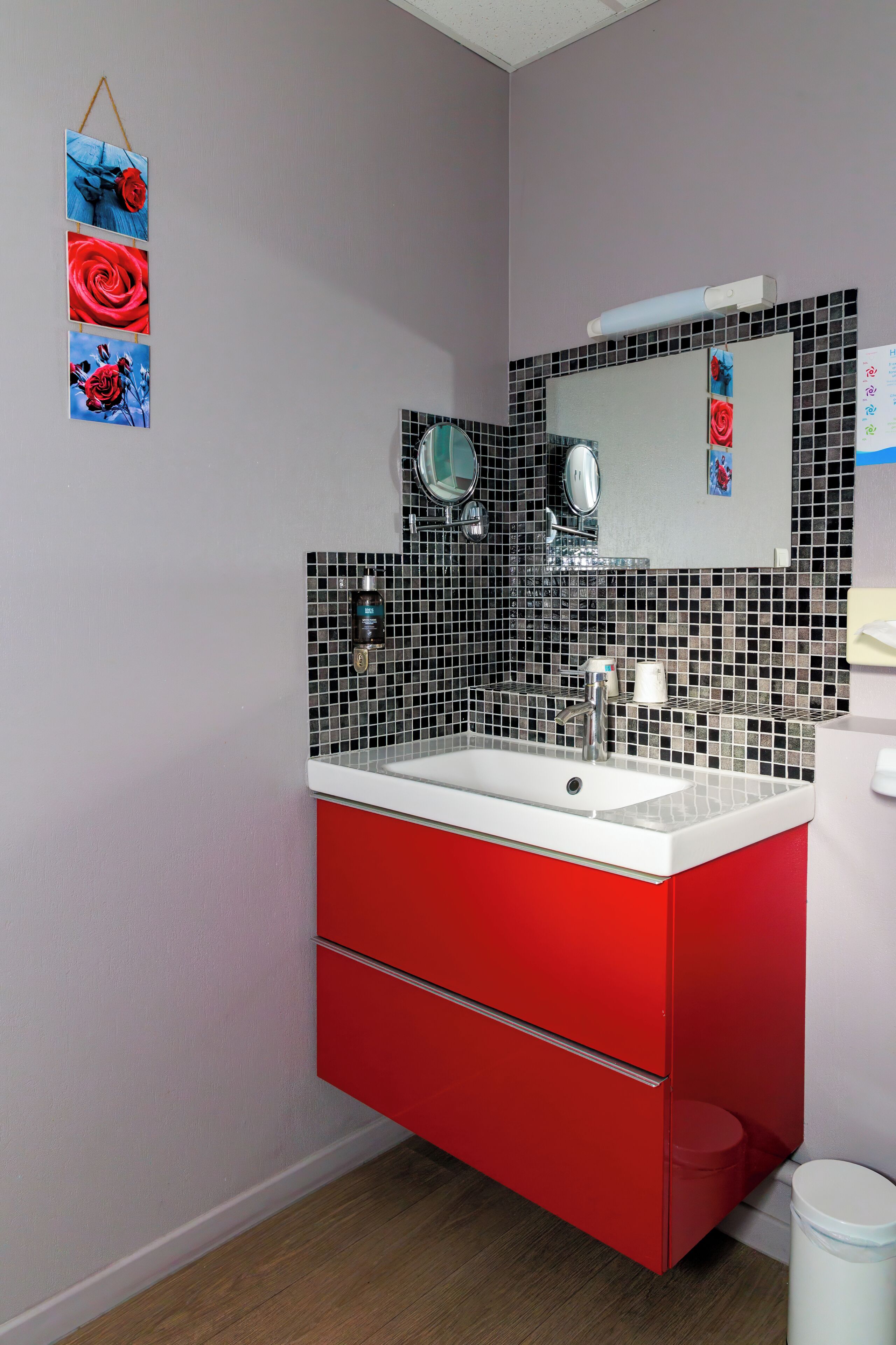 Un baño con tocador rojo, lavamanos blanco, espejo y un salpicadero de mosaicos.