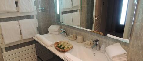 A modern bathroom with a large mirror, white towels, a sink, and a basket of toiletries.