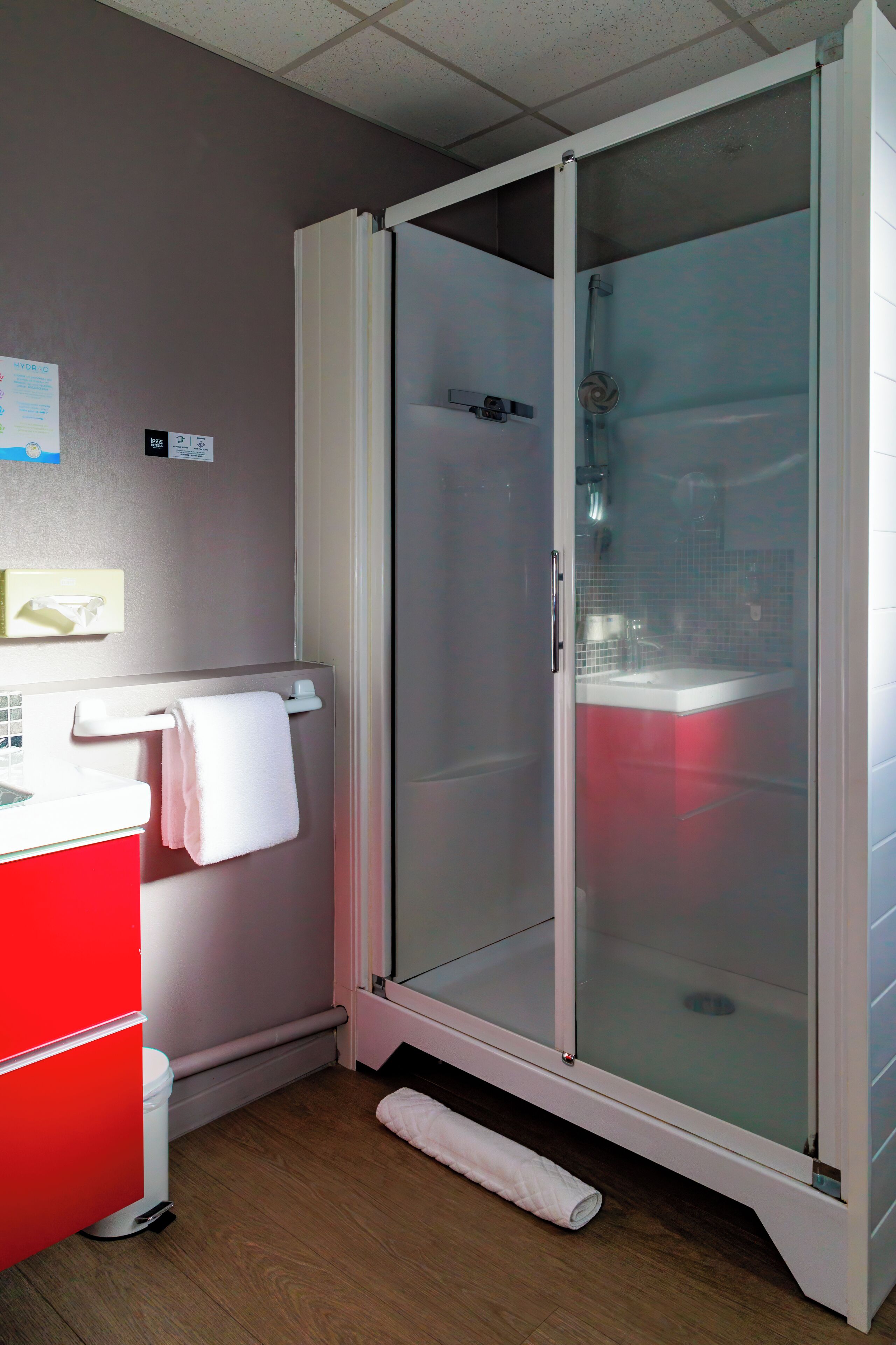 A bathroom with a glass-enclosed shower, a red sink, and a white towel hanging on the wall.