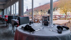 A restaurant with tables set for dining, large windows offering a view of a town and hills. - Logis Central Hôtel & Spa (Bort-les-Orgues)