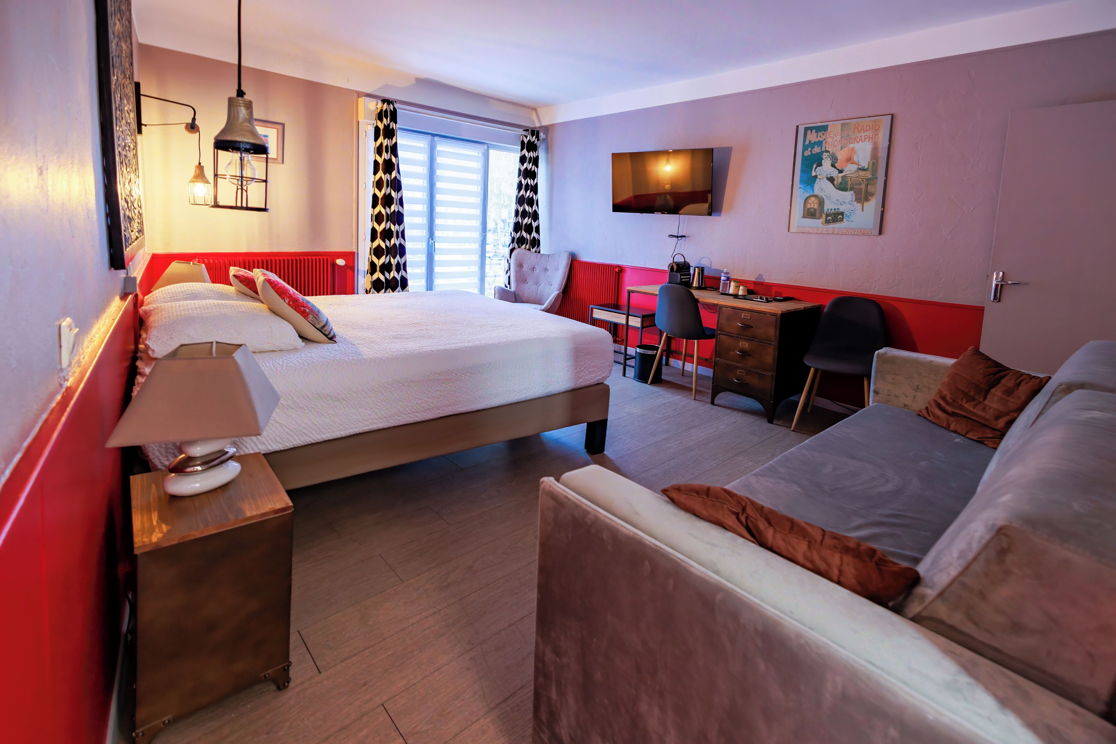 Habitación de hotel con una cama grande, un escritorio, una silla, un televisor y una ventana con cortinas.