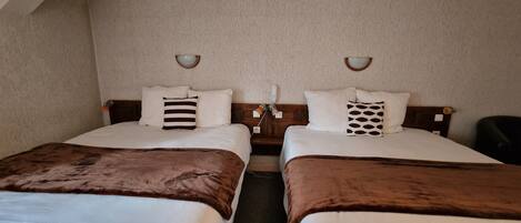 Habitación de hotel con dos camas individuales, cada una con una manta marrón y ropa de cama blanca. Hay dos lámparas de pared y una mesita entre las camas.