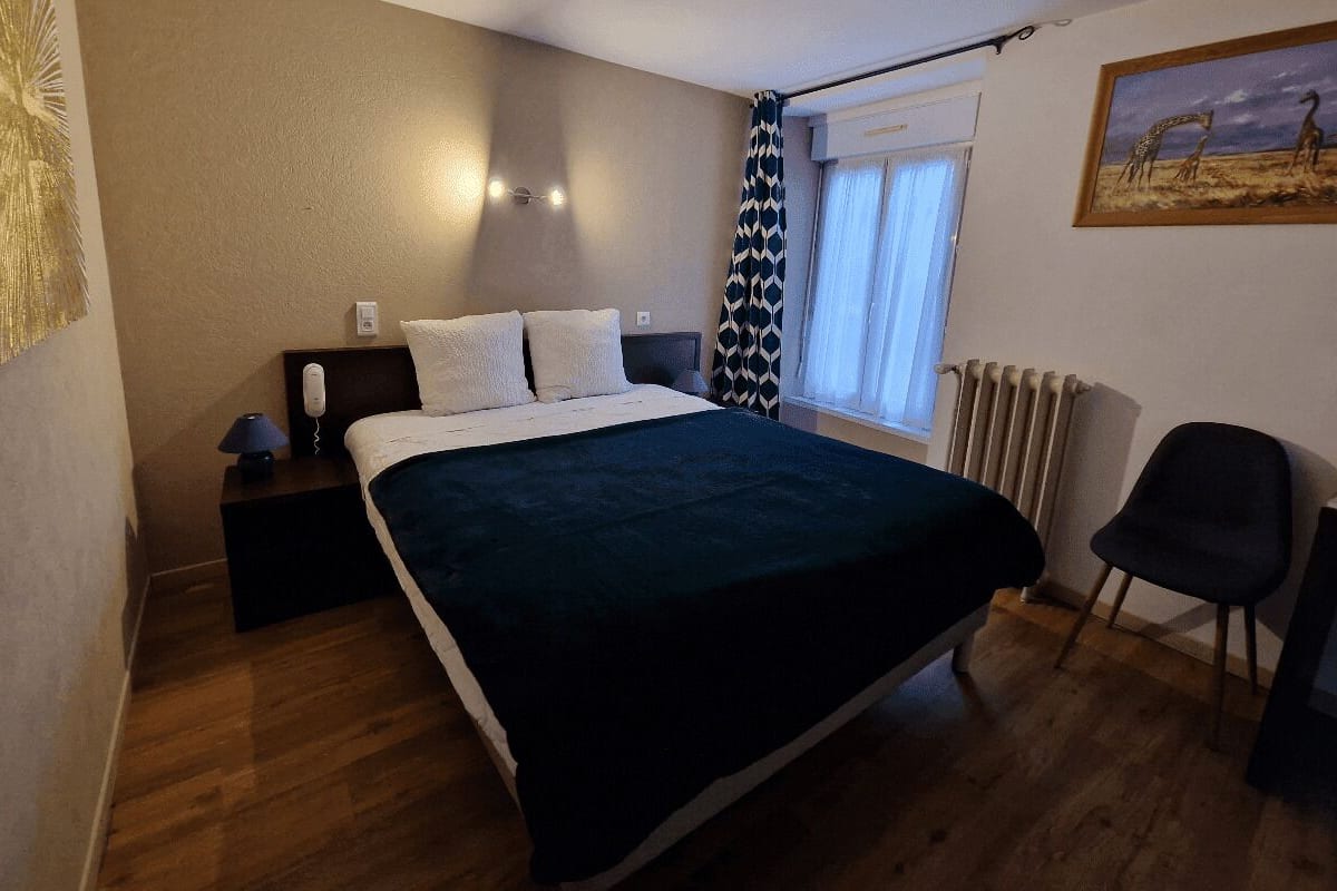 A bedroom with a bed, bedside table, lamp, and a painting on the wall.