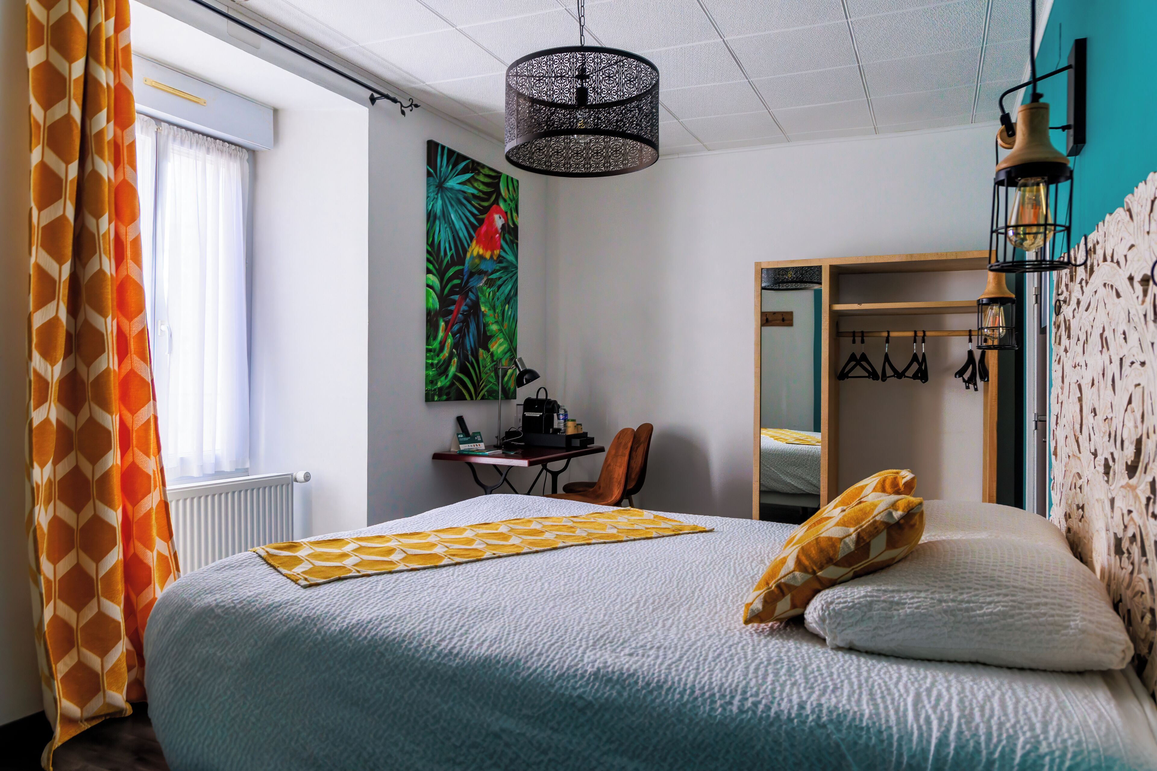 Un dormitorio con cama, escritorio, silla, lámpara colgante y un espejo grande.
